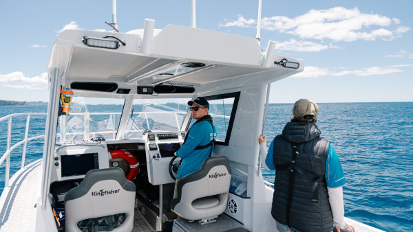 Man skippering a boat with a crew member pictured from behind on the right